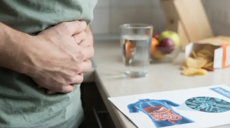 Persona con le mani sullo stomaco accanto a un bicchiere d'acqua e un'immagine del tratto intestinale.
