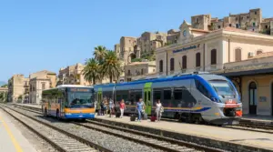 Stazione ferroviaria in Sicilia con treno Trenitalia e autobus SAIS, passeggeri con valigie sulla banchina