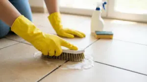 Persona con guanti gialli che pulisce le fughe delle piastrelle con una spazzola